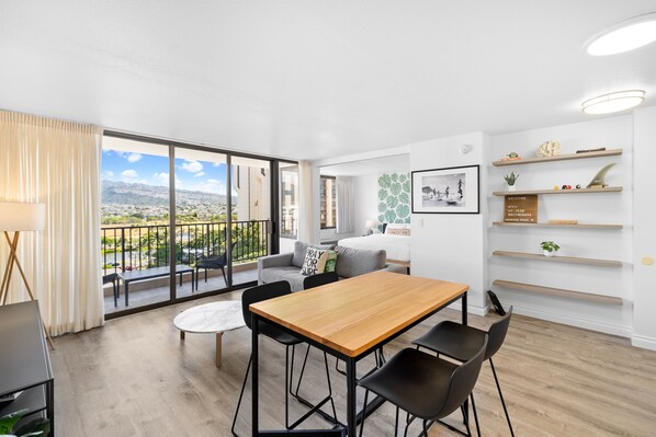 Ein modernes Wohnzimmer mit einem Holzesstisch, schwarzen Stühlen, einem grauen Sofa und einem Balkon mit Blick auf die Stadt.