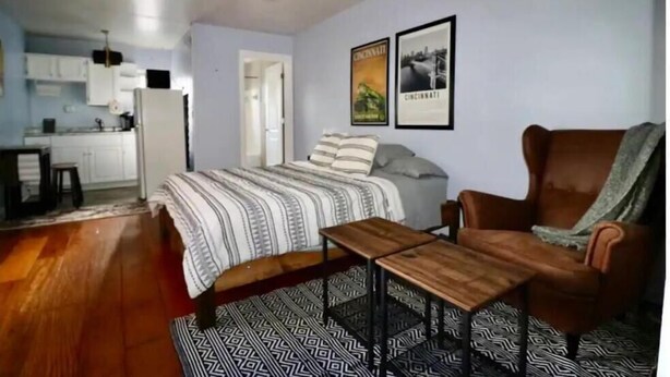 Een slaapkamer met een bed, een houten tafel, een bruine fauteuil en een kamerkleed met dessin.