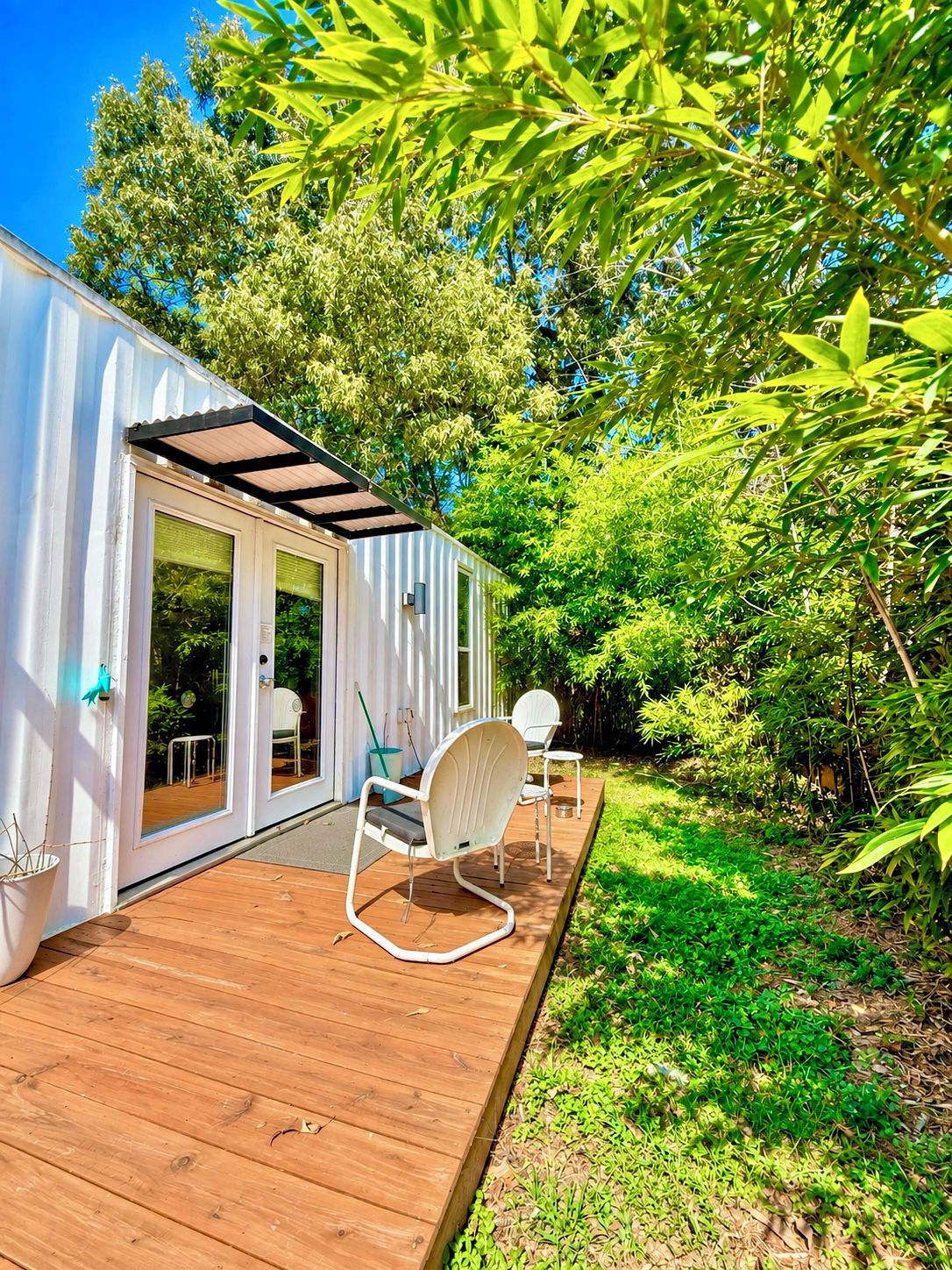 A white building with a wooden deck, two white chairs, and a small table.