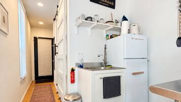 A compact kitchenette with a refrigerator, sink, and storage shelves.