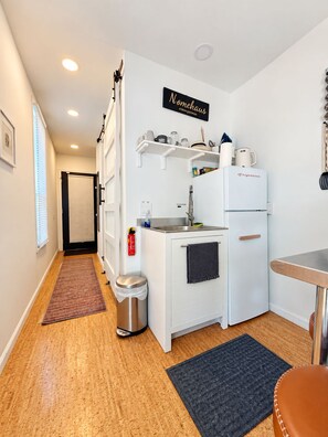 Una kitchenette compacta con refrigerador, pileta y estanterías.