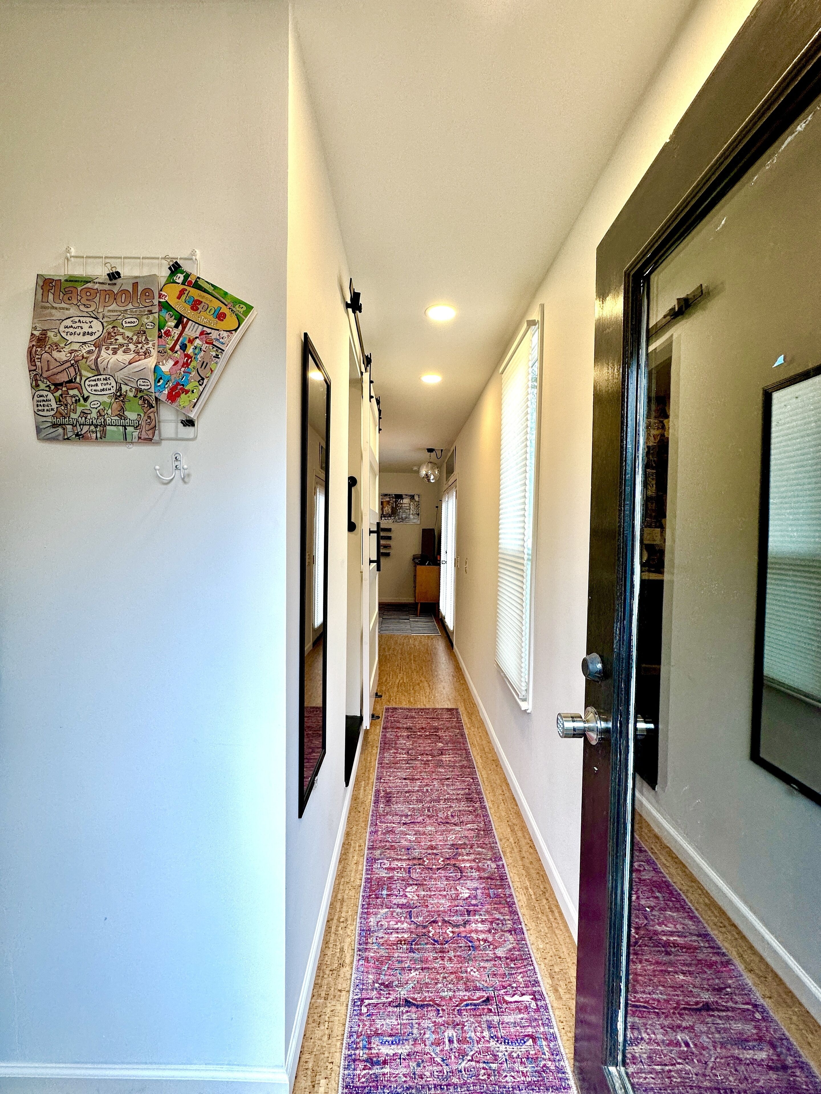 A hallway with a purple carpet, a bulletin board with comics, and a door with a glass panel.