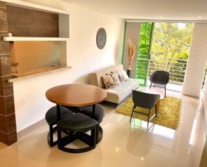 Relax in this stylish living room with a sofa, coffee table, and chairs, offering a view of lush greenery outside.