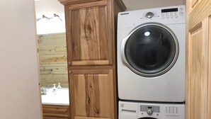 Un angolo lavanderia con lavatrice e asciugatrice affiancate, mobili contenitori in legno e una finestra vista all'esterno.