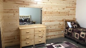 Una camera da letto con pareti rivestite in legno, un comò in legno con cassetti, un letto con copriletto decorato e uno specchio appeso al muro.