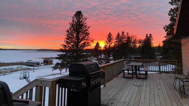 Un terrazzo in legno con una griglia per barbecue, posti a sedere all'aperto e vista sul tramonto sull'acqua.