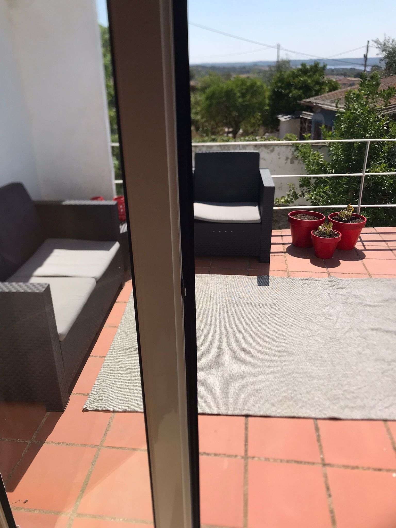 Een balkon met een zwarte bank, een klein tafeltje en drie rode planten in potten.