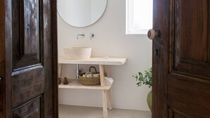 A bathroom with a wooden door, a round mirror, a white sink, and a window.