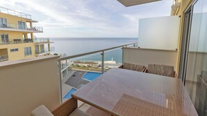 Un balcó amb vista al mar, una piscina i edificis veïnals.