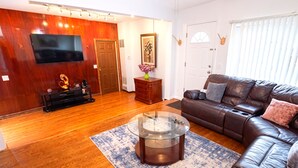 A living room with a leather sofa, a glass coffee table, a flat-screen TV, wooden flooring, and a door with a decorative item. - Amazing Mid-Term Rental Entire Home In Glenview (Northbrook)