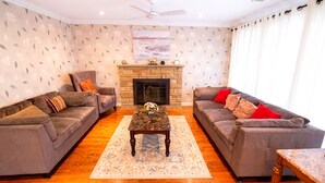 A living room with two sofas, a fireplace, a ceiling fan, and a large window. - Amazing Mid-Term Rental Entire Home In Glenview (Northbrook)