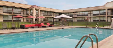 A swimming pool with lounge chairs and umbrellas, surrounded by a building with multiple balconies.