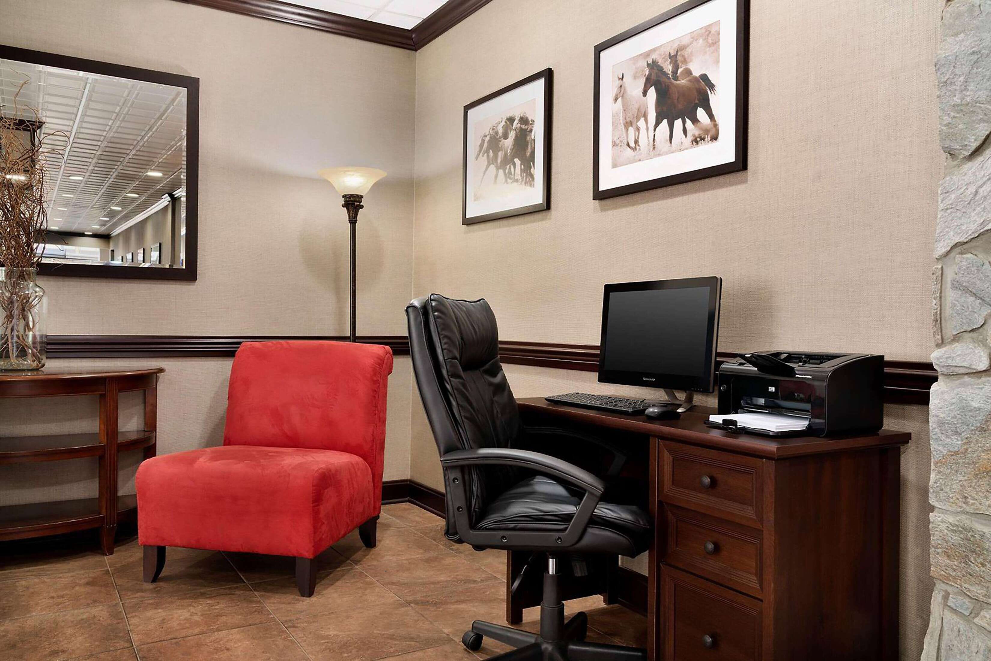Un bureau d’hôtel avec un bureau, deux chaises, un ordinateur et des tableaux encadrés accrochés au mur.