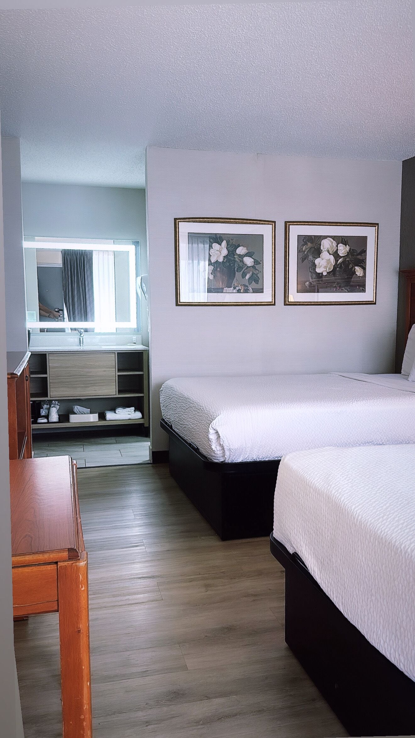 Une chambre d’hôtel avec un lit, un bureau, un miroir et deux tableaux encadrés accrochés au mur.