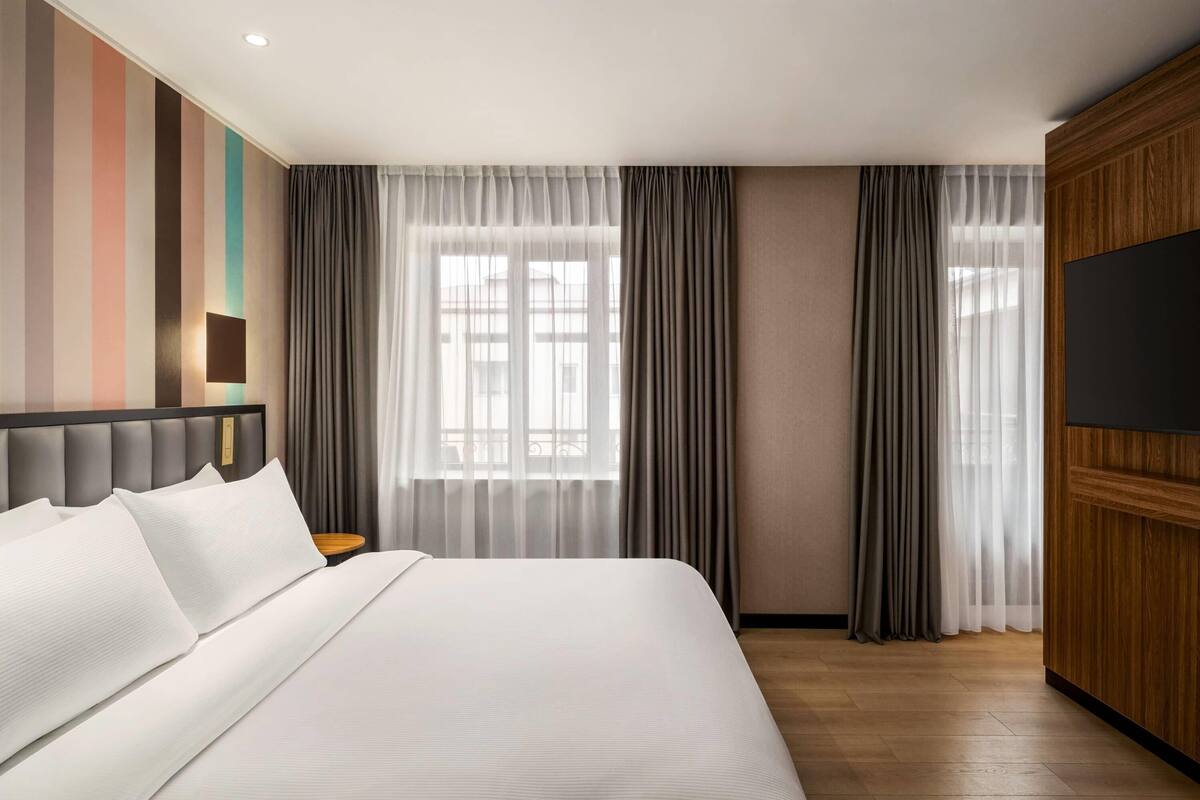 A hotel room with a large bed, a flat-screen TV, and a window with curtains.