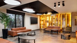 A modern lounge area with leather sofas, round tables, and a large TV screen. - Ramada Encore By Wyndham Tashkent (Tashkent)