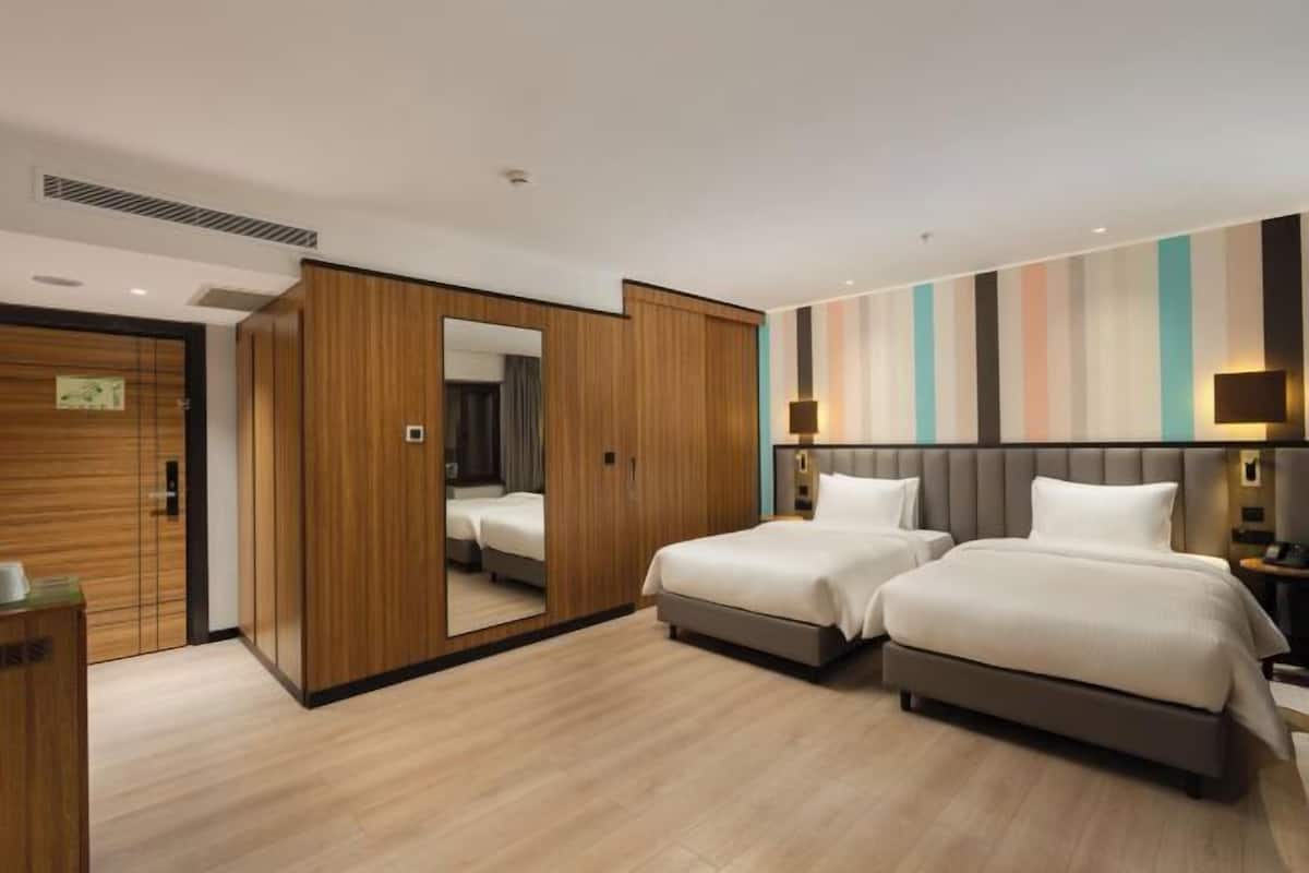 A hotel room with two beds, a wardrobe, a mirror, and a striped wall.