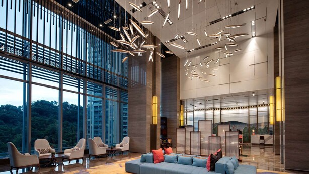 A spacious lobby with a large seating area, modern lighting fixtures, and large windows offering a view of the outdoors. - Wyndham Garden Foshan Jinshazhou (Guangzhou)