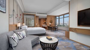 A modern hotel room with a bed, sofa, desk, and a large window offering a city view. - Wyndham Garden Foshan Jinshazhou (Guangzhou)