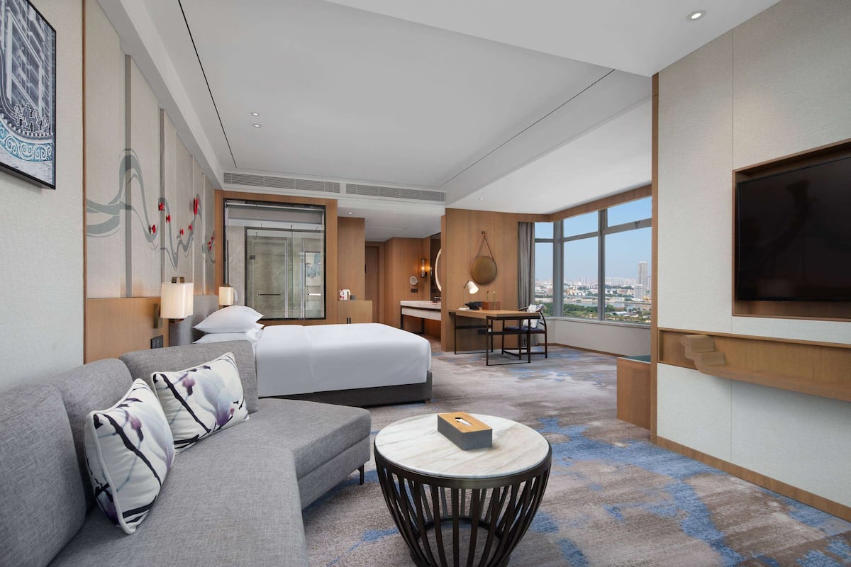 Habitación de hotel moderna con cama, sofá, escritorio y un amplio ventanal con vista a la ciudad.