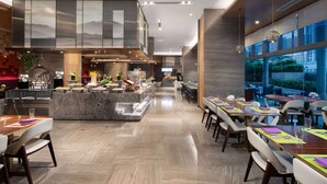 A modern restaurant with a central island, long dining tables, and a view of the outdoors through large windows. - Wyndham Garden Foshan Jinshazhou (Guangzhou)