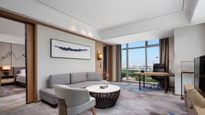 A modern hotel room with a large window, a sofa, a round coffee table, a desk with a chair, and a TV. - Wyndham Garden Foshan Jinshazhou (Guangzhou)