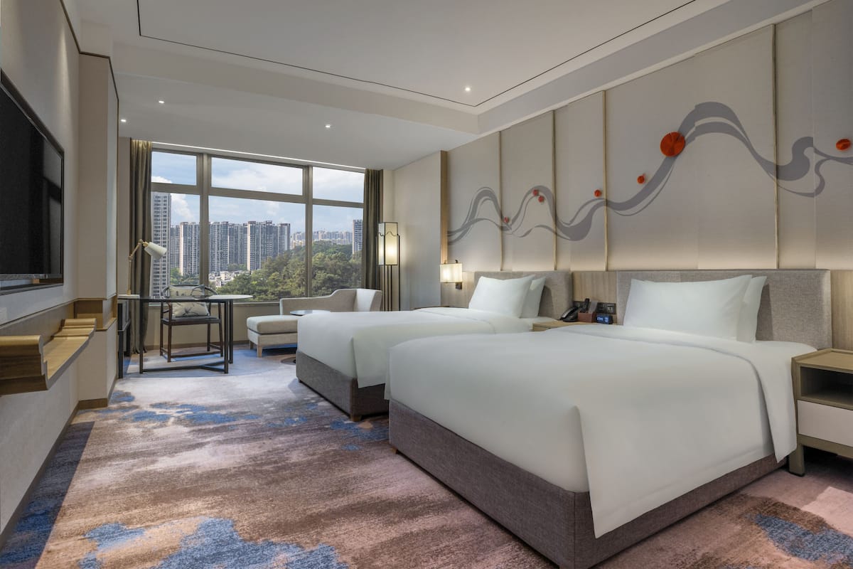 Habitación de hotel con dos camas, un ventanal con vistas a la ciudad, un escritorio y una silla.