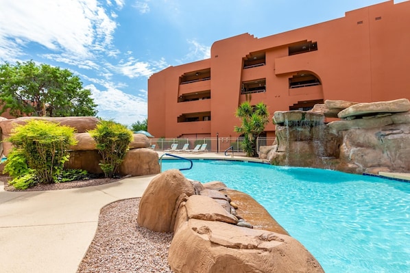 A hotel with a swimming pool surrounded by rock formations and greenery.