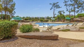 Un área de piscina con sillones de descanso y sombrillas, rodeada de árboles y jardines.