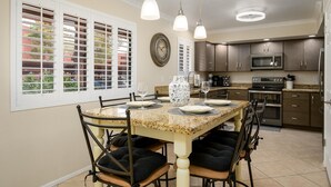 Una cocina con una mesa de comedor dispuesta para cuatro personas, equipada con electrodomésticos modernos y un jarrón decorativo.