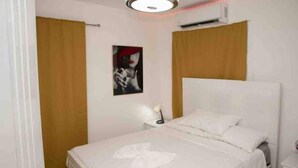 Ein Schlafzimmer mit einem Bett, einem Nachttisch, einer Wand-Klimaanlage und einem Poster an der Wand.