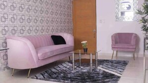 Ein Wohnzimmer mit einem rosa Sofa, einem kleinen Tisch mit einem Topfpflanzen, einem grauen Teppich und einer Holztür.