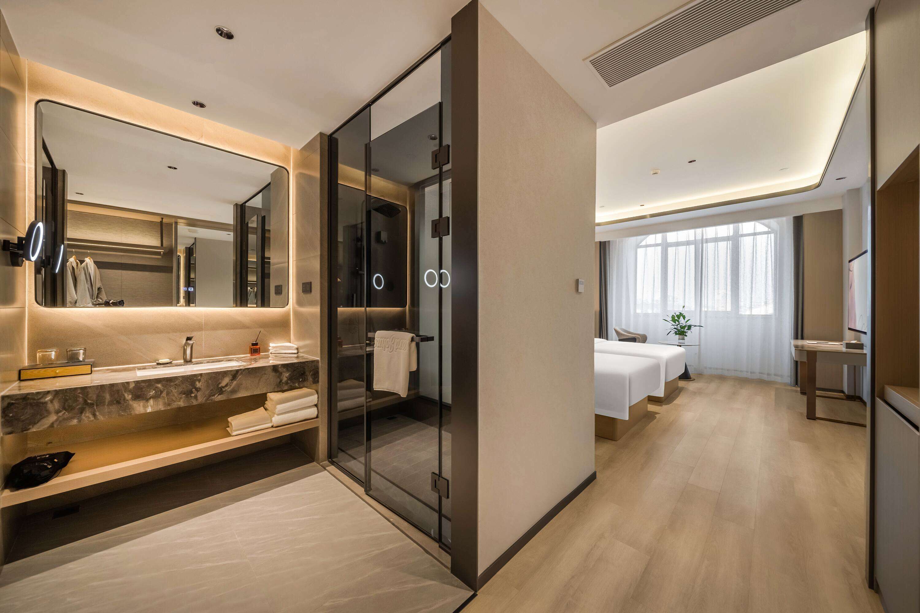 Un baño de hotel moderno con ducha de vidrio, tocador de mármol y un espejo grande.