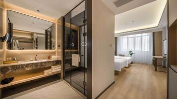 Un baño de hotel moderno con ducha de vidrio, tocador de mármol y un espejo grande.