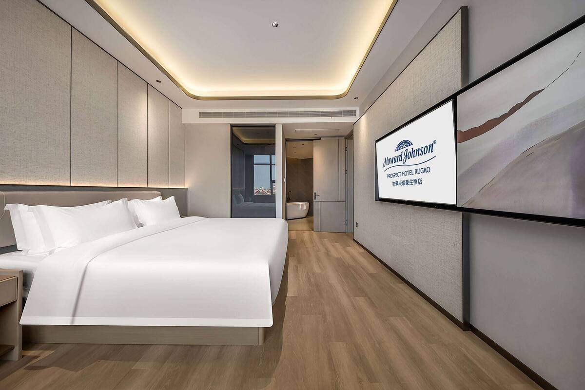 Habitación de hotel moderna con una cama grande, un televisor de pantalla plana y vistas a la ciudad.