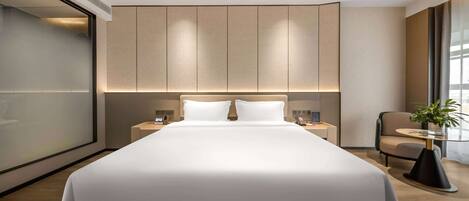 Una habitación de hotel moderna con una cama grande, mesitas de noche, una silla y una planta en maceta.