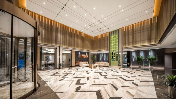 A spacious lobby with a geometric marble floor, modern furniture, and vertical wooden slats on the ceiling.