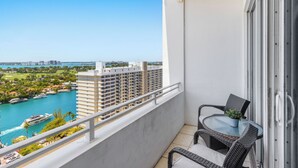 A balcony with a view of a marina and buildings, a wicker chair, and a potted plant. - Castle PH11 Penthouse with bay views, Balcony, Pool, Gym & Free parking. Steps from the beach. (Miami Beach)