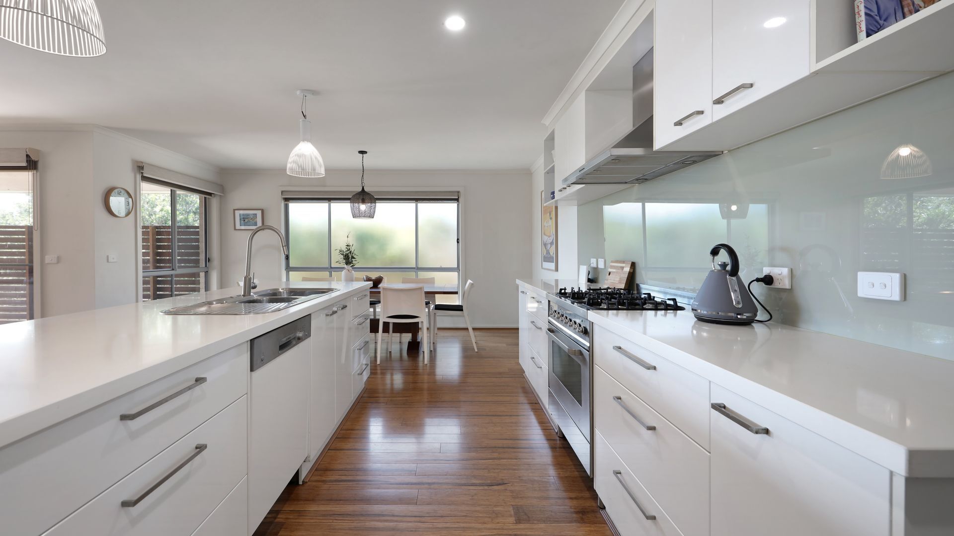 Une cuisine moderne avec des meubles blancs, un îlot central, des appareils en acier inoxydable et des luminaires suspendus.
