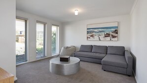 A living room with a grey sofa, a round coffee table, and a beach scene painting on the wall. - Bayview Bliss in Surf Beach (Surf Beach)