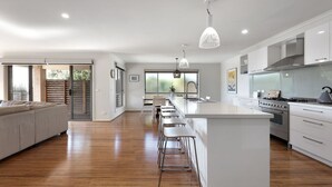 A modern kitchen with a central island, bar stools, and a dining area with a sofa. - Bayview Bliss in Surf Beach (Surf Beach)