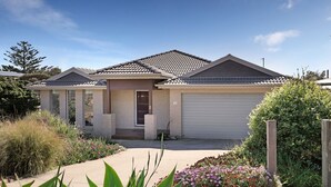 A single-story house with a tiled roof, a garage, and a front yard with various plants and flowers. - Bayview Bliss in Surf Beach (Surf Beach)