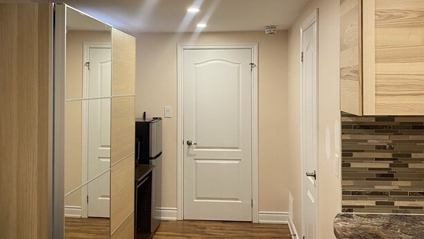 A hallway with wooden flooring, a white door, and a kitchen area with a granite countertop. - Lovely one bedroom unit  (Mississauga)