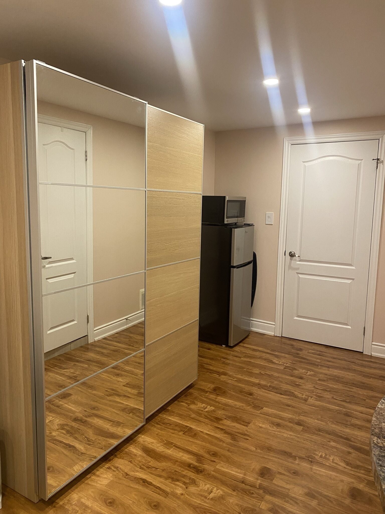 Een kamer met een schuifdeurkast, een koelkast en een magnetron erboven.