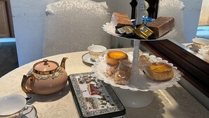 Un juego de té con tetera y tazas sobre una mesa, una bandeja con pasteles y un plato decorativo.