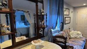 Una habitación acogedora con una mesa redonda cubierta con un mantel blanco, un sofá floral y un espejo grande que refleja la habitación.