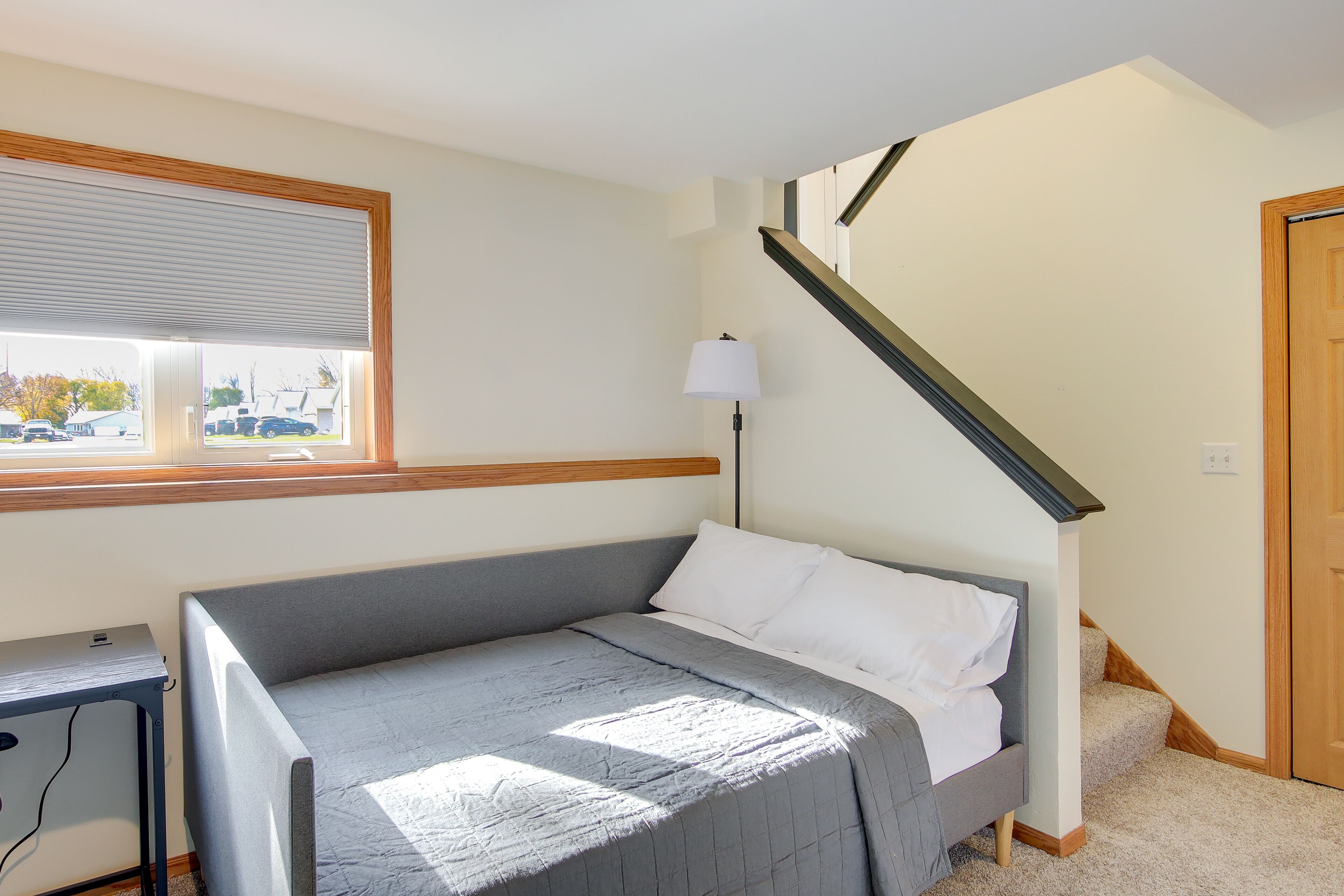 A bedroom with a bed, a desk, a lamp, a window, and a staircase.