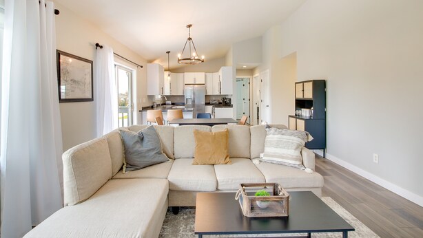 A modern living room with a sectional sofa, a coffee table, and a kitchen in the background. - Bright Little Chute Condo w/ Deck & Yard! (Little Chute)
