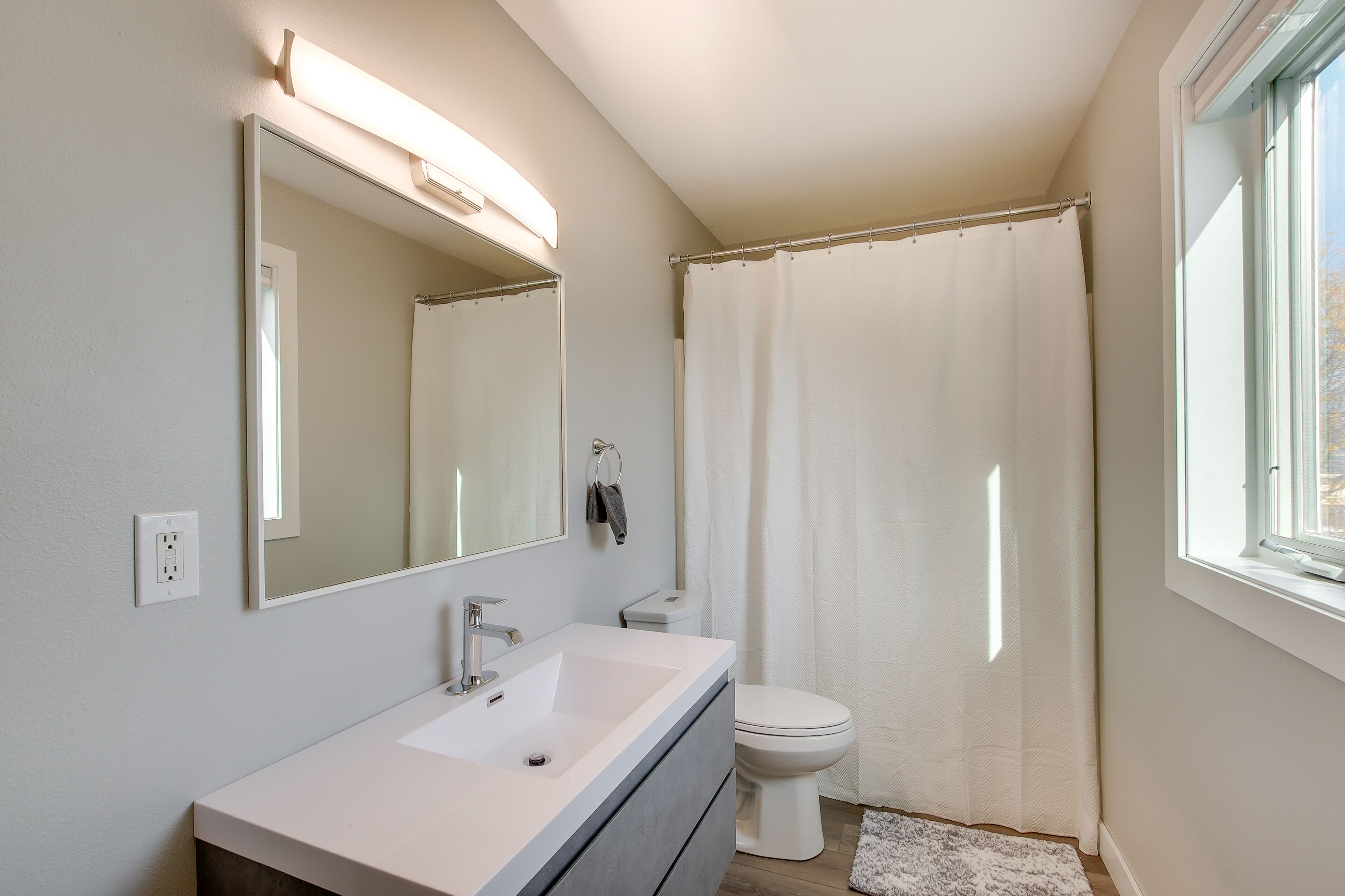 Un baño con lavamanos blanco, espejo, inodoro y cortina de ducha.