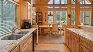 Une cuisine dotée de meubles en bois, de plans de travail en granit, d’un coin repas avec des chaises et d’une vue dégagée grâce à de grandes fenêtres.